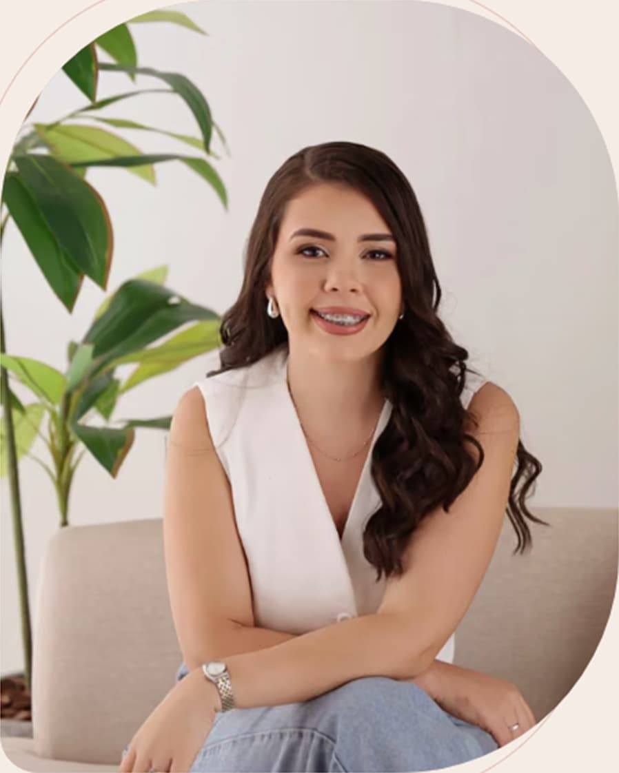 Simone Lima sentada em um sofá claro, ao lado de uma planta